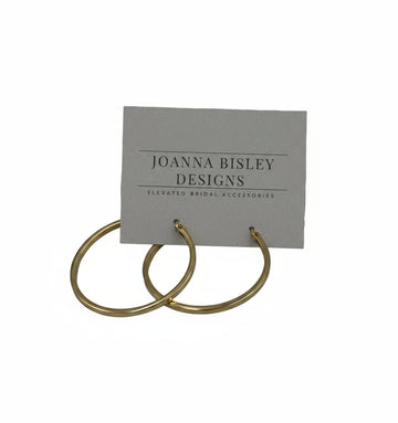 Gold hoop earrings on a Joanna Bisley Designs card against a gray background